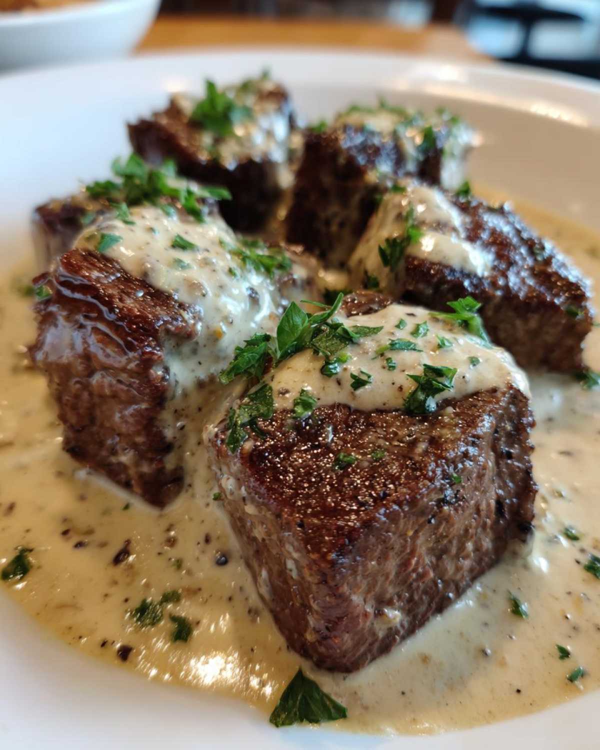 Close-up of seared Keto Creamy Peppercorn Steak Bites covered in a rich, creamy sauce and fresh parsley.