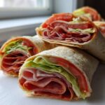 Several cross-sections of Keto Italian Sub Roll-Ups showing layers of deli meat, lettuce, and tomato wrapped in a tortilla.