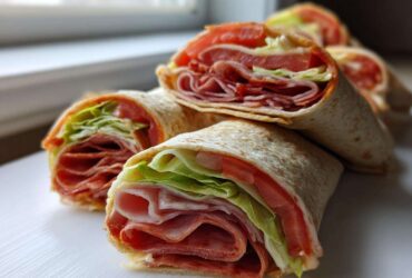 Several cross-sections of Keto Italian Sub Roll-Ups showing layers of deli meat, lettuce, and tomato wrapped in a tortilla.