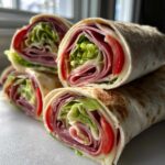 Close-up of stacked Keto Italian Sub Roll-Ups showing layers of deli meat, cheese, lettuce, and tomato inside a tortilla.