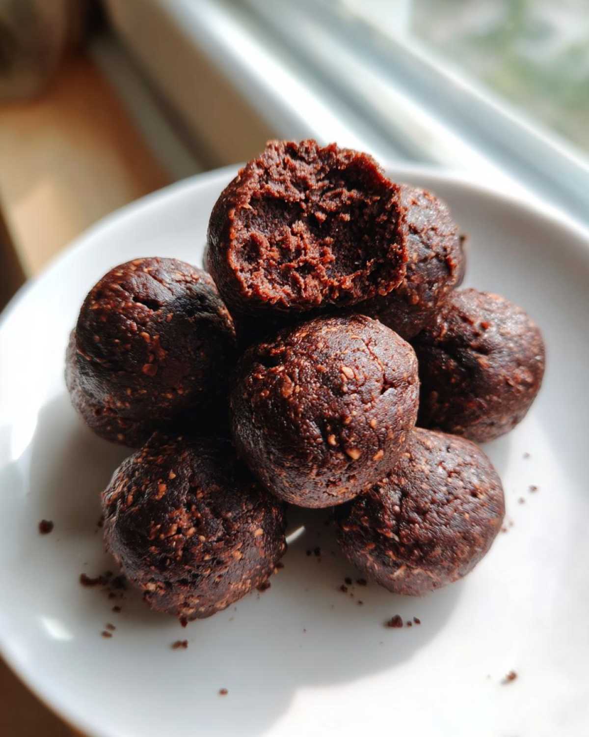 A stack of fudgy No-Bake Brownie Batter Protein Balls on a white plate, one is bitten into.