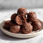 A stack of rich, dark No-Bake Chocolate Chip Cookie Dough Truffles dusted with cocoa powder, one cut open.