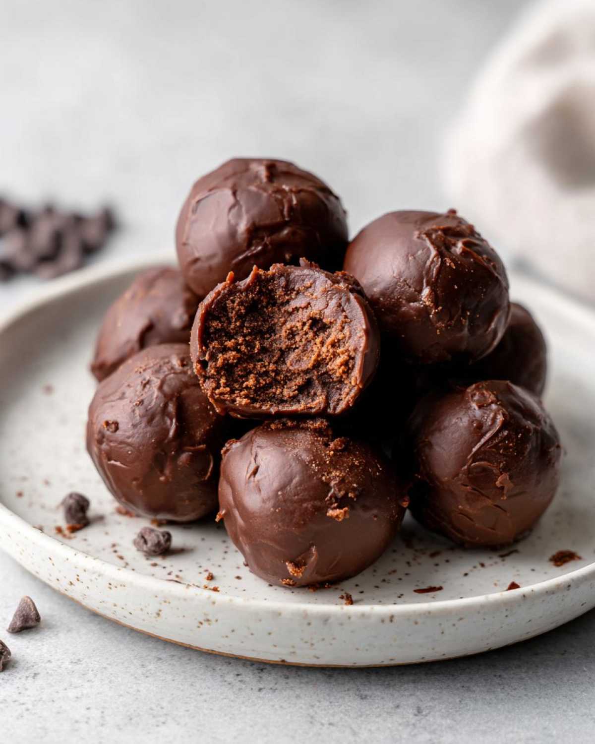 A stack of rich, chocolate-covered No-Bake Chocolate Chip Cookie Dough Truffles, one cut open to show the doughy center.