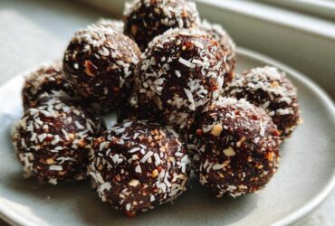 A close-up of several No-Bake Chocolate Hazelnut Crunch Balls rolled in shredded coconut on a light gray plate.