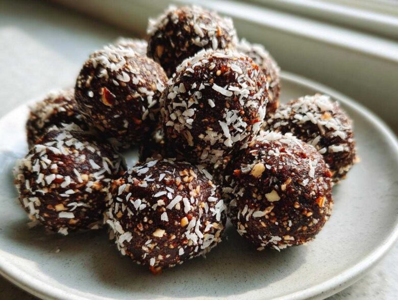 A close-up of several No-Bake Chocolate Hazelnut Crunch Balls rolled in shredded coconut on a light gray plate.