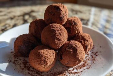 A stack of rich, dark No-Bake Chocolate Orange Truffles generously dusted with cocoa powder on a white plate.