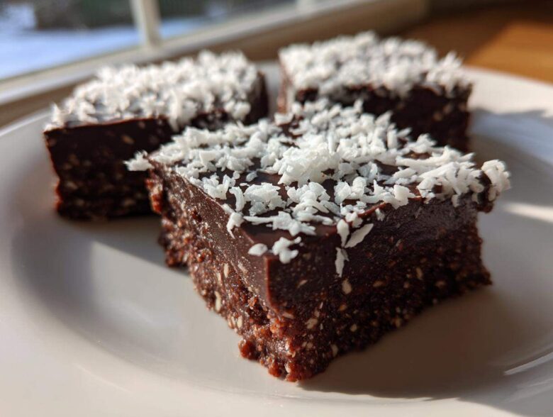 Three squares of rich, dark No-Bake Coconut Chocolate Date Bars topped with shredded coconut.