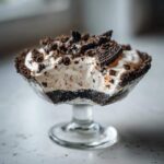 A single serving of No-Bake Cookies and Cream Pie Cups in a glass dish, topped with crushed cookies.