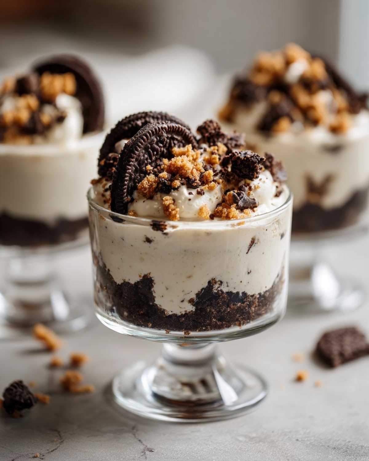 Close-up of a No-Bake Cookies and Cream Pie Cups dessert in a glass dish, topped with cookie crumbs and a whole cookie.