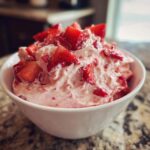 A white bowl filled with fluffy, pink No-Bake Strawberry Cheesecake Dip topped with fresh, diced strawberries.