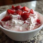 A close-up of fluffy No-Bake Strawberry Cheesecake Dip topped with fresh strawberry pieces in a white bowl.