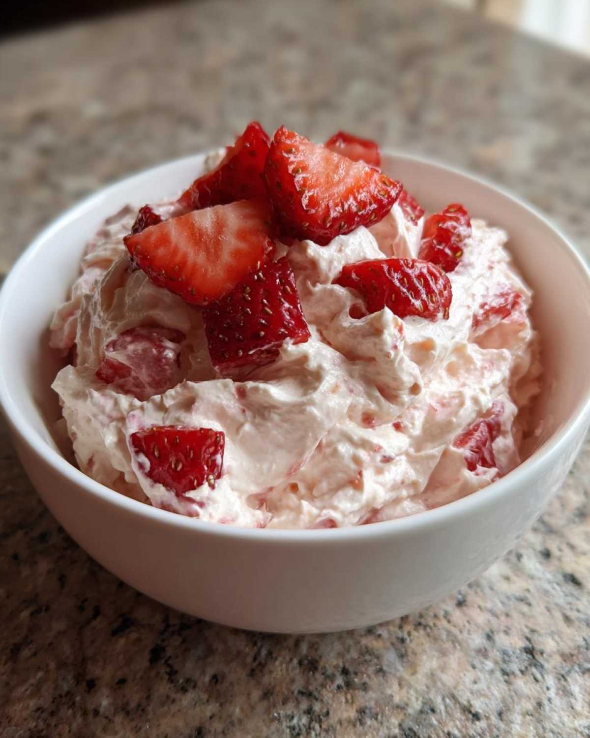 A white bowl filled with fluffy No-Bake Strawberry Cheesecake Dip, topped with fresh strawberry slices.