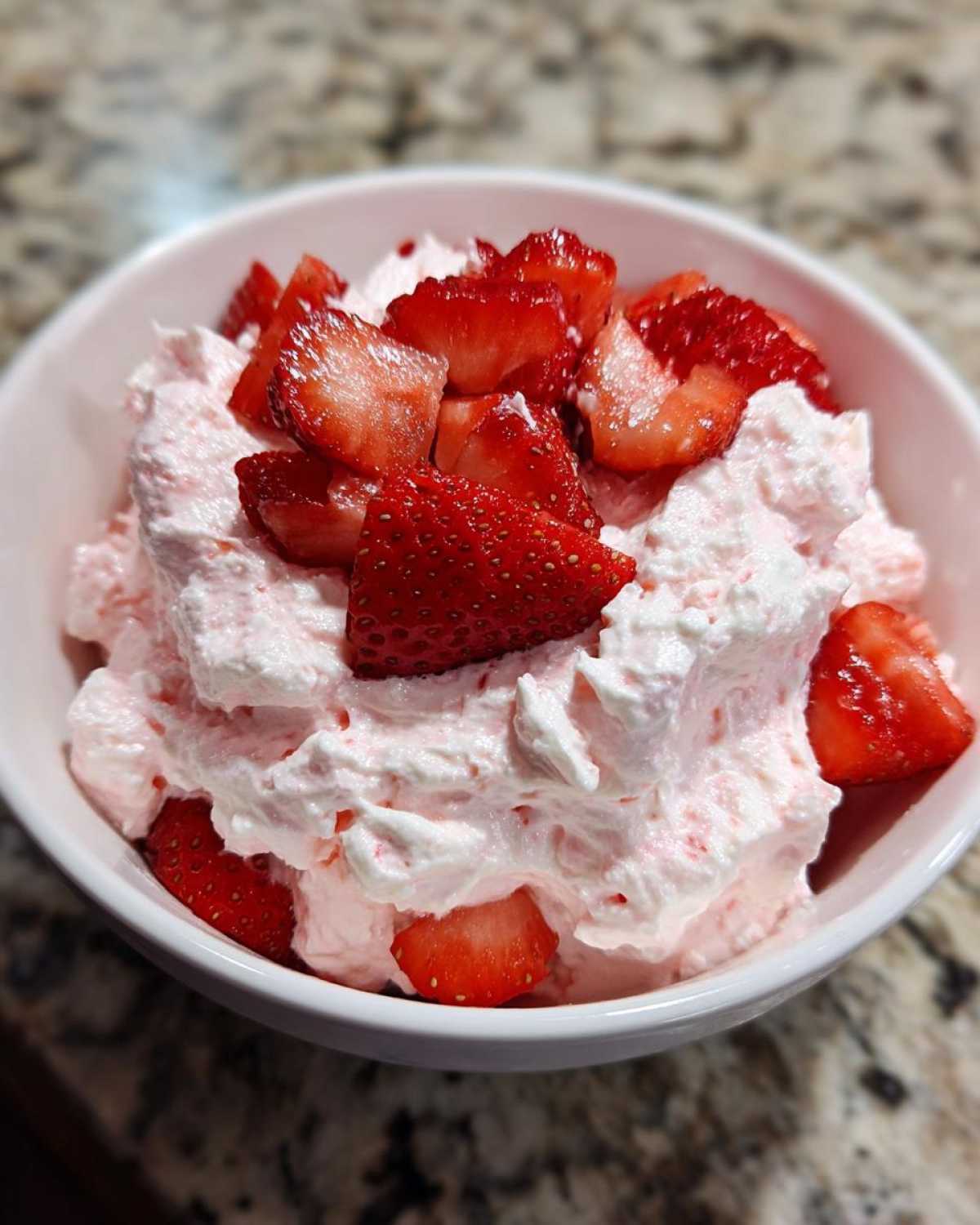 A white bowl filled with fluffy pink No-Bake Strawberry Cheesecake Dip, topped generously with fresh, sliced strawberries.