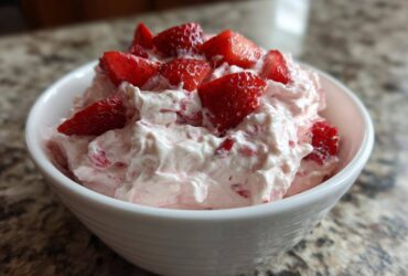 A close-up of fluffy No-Bake Strawberry Cheesecake Dip topped with fresh strawberry pieces in a white bowl.