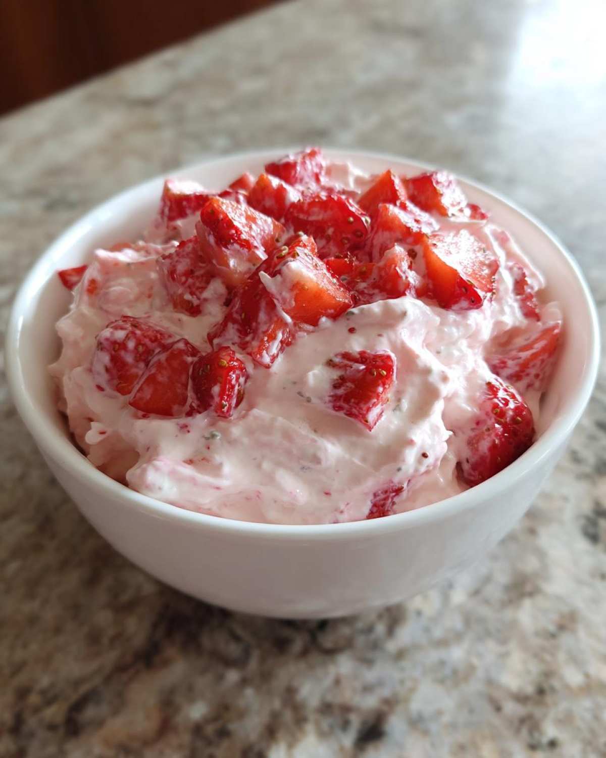 A white bowl filled with pink No-Bake Strawberry Cheesecake Dip topped generously with fresh, chopped strawberries.