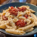 A close-up of One-Pot Creamy Goat Cheese Pasta with roasted tomatoes in a teal bowl.