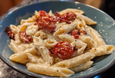 A close-up of One-Pot Creamy Goat Cheese Pasta with roasted tomatoes in a teal bowl.