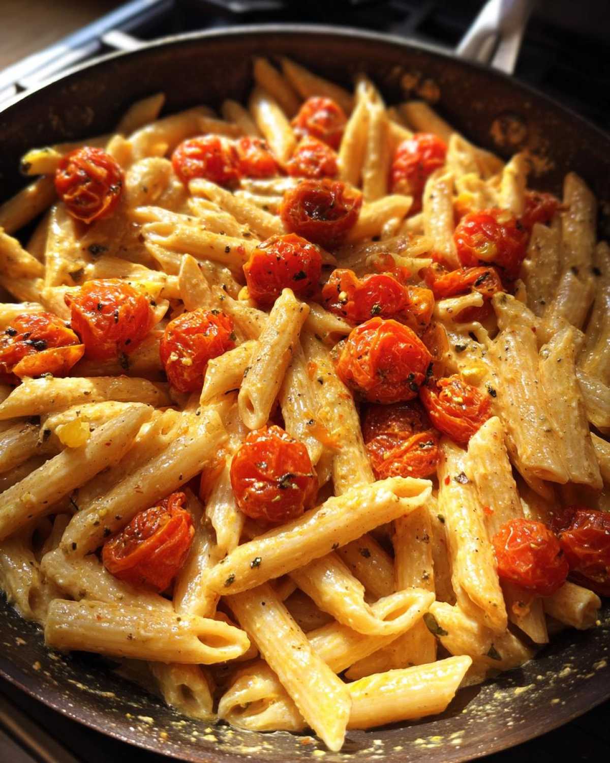 Close-up of One-Pot Creamy Goat Cheese Pasta mixed with roasted cherry tomatoes in a dark skillet.
