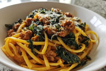 A close-up view of a serving of One-Pot Spicy Sausage and Kale Pasta topped with grated cheese in a white bowl.