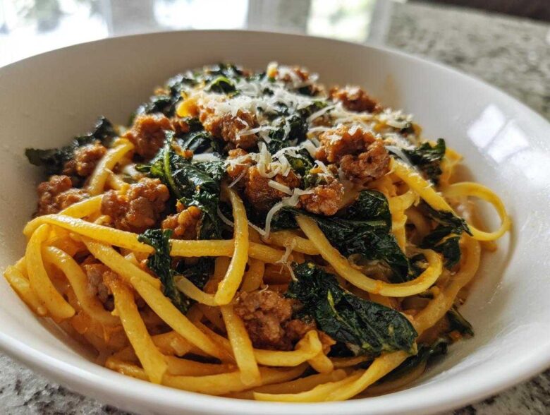 A close-up view of a serving of One-Pot Spicy Sausage and Kale Pasta topped with grated cheese in a white bowl.