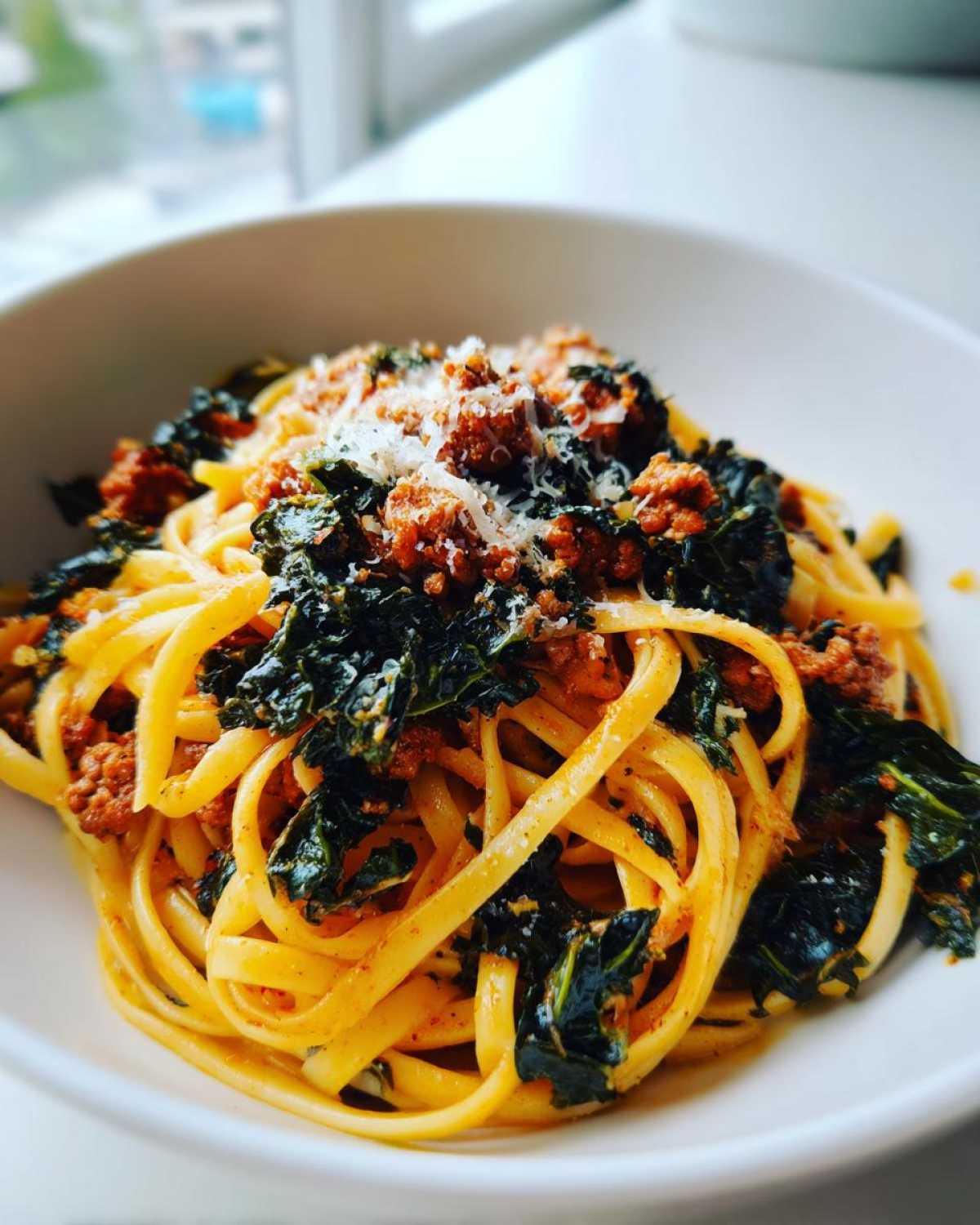 A close-up of a bowl filled with One-Pot Spicy Sausage and Kale Pasta, topped with grated cheese.