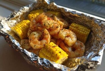 Close-up of seasoned shrimp and corn on the cob pieces cooked inside a shiny aluminum foil packet.