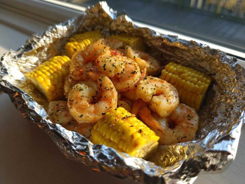 Close-up of seasoned shrimp and corn on the cob pieces cooked inside a shiny aluminum foil packet.