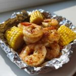 Close-up of seasoned shrimp and corn on the cob pieces cooked inside a foil packet.