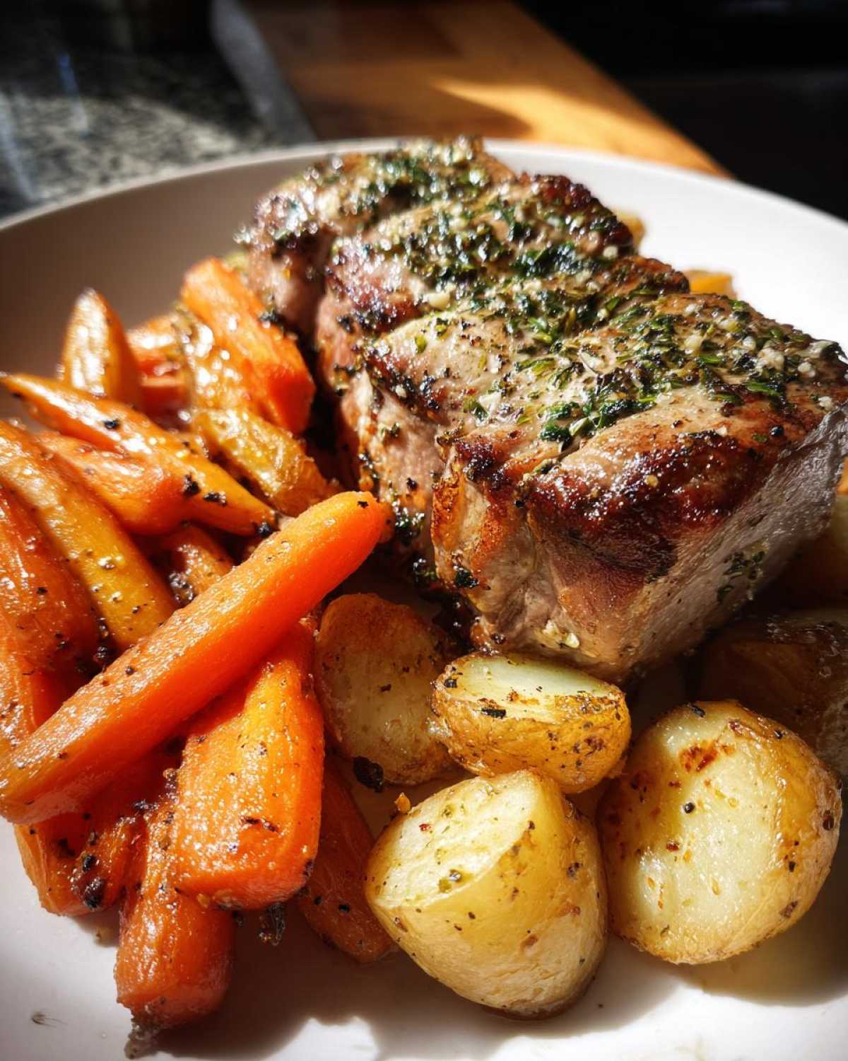 Close-up of sliced Sheet Pan Garlic Herb Pork Tenderloin served with roasted carrots and potatoes.