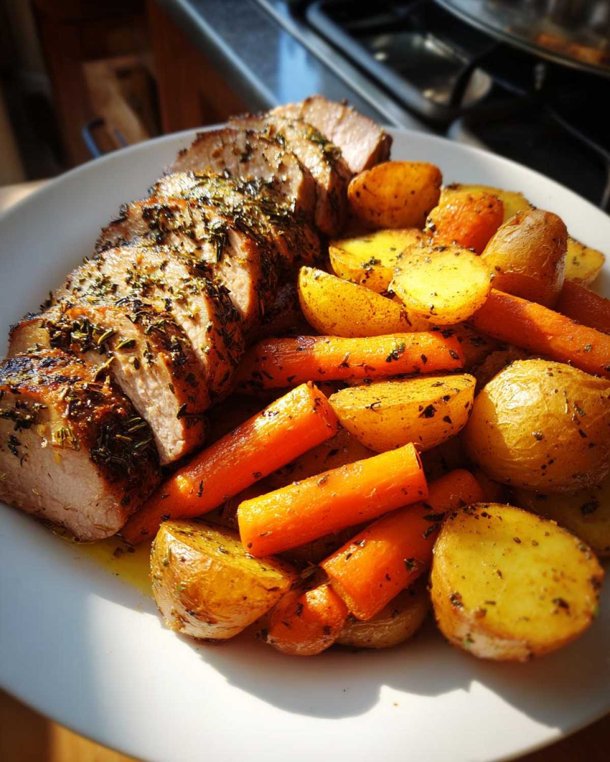 Sliced Sheet Pan Garlic Herb Pork Tenderloin served with roasted carrots and potatoes on a white plate.