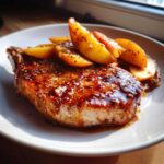 Close-up of a thick, juicy Sheet Pan Maple Dijon Pork Chop topped with a glossy glaze and caramelized apple slices.