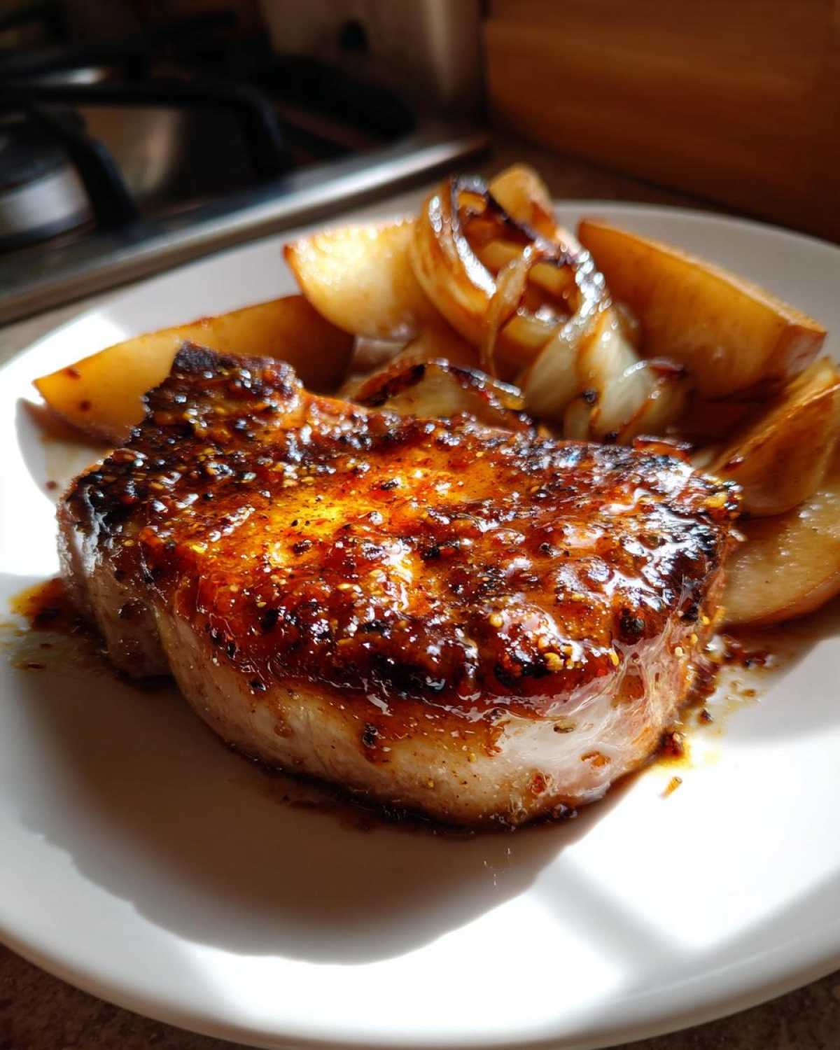 Close-up of a juicy pork chop glazed with maple dijon sauce, served with roasted apples and onions.
