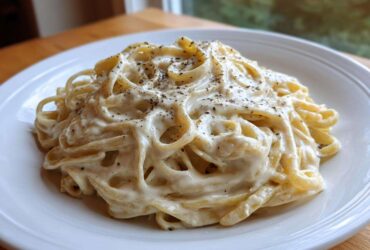 A close-up of fettuccine pasta generously coated in Vegan Creamy Cashew Alfredo Sauce, topped with black pepper.