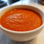 Close-up of a white bowl filled with vibrant orange Vegan Creamy Tomato Coconut Soup.