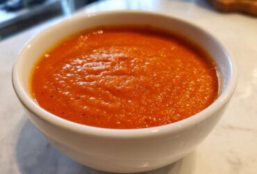Close-up of a white bowl filled with vibrant orange Vegan Creamy Tomato Coconut Soup.