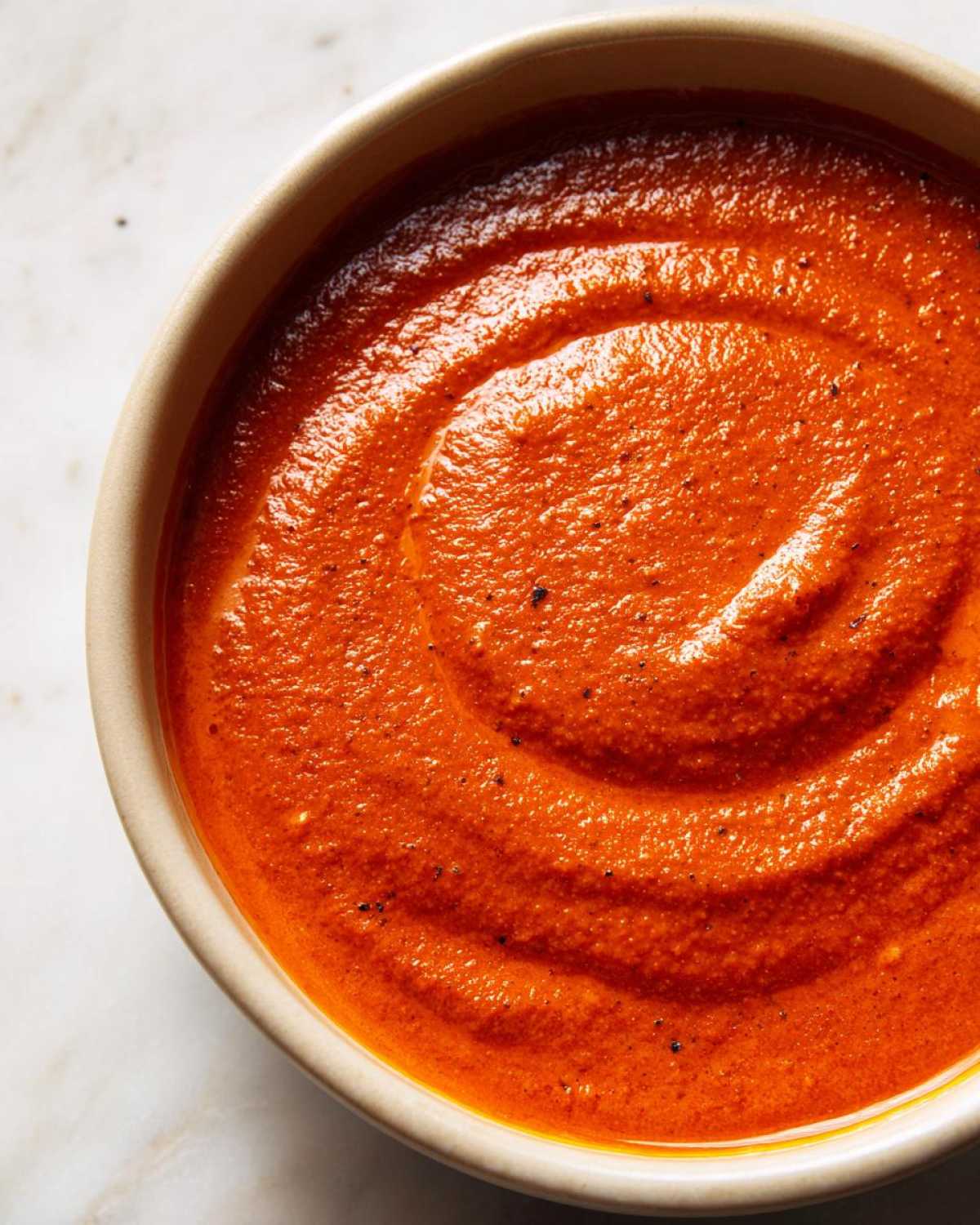 A close-up, overhead shot showing the rich, thick texture of Vegan Creamy Tomato Coconut Soup swirled in a light-colored bowl.