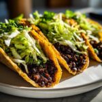A row of crispy tacos filled with seasoned black beans and topped with shredded cilantro lime slaw.