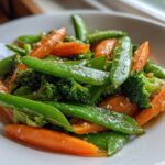 Close-up of a bright Vegan Spring Vegetable Stir Fry featuring snap peas, carrots, and broccoli, topped with sesame seeds.