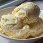 Close-up of three scoops of creamy, pale yellow banana ice cream served in a white bowl.