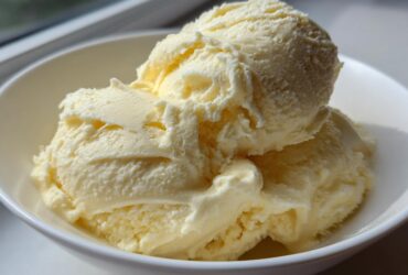 Close-up of three scoops of creamy, pale yellow banana ice cream served in a white bowl.