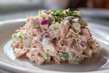 A mound of creamy salmon salad mixed with diced celery and red onion, topped with fresh chives, ready to eat.