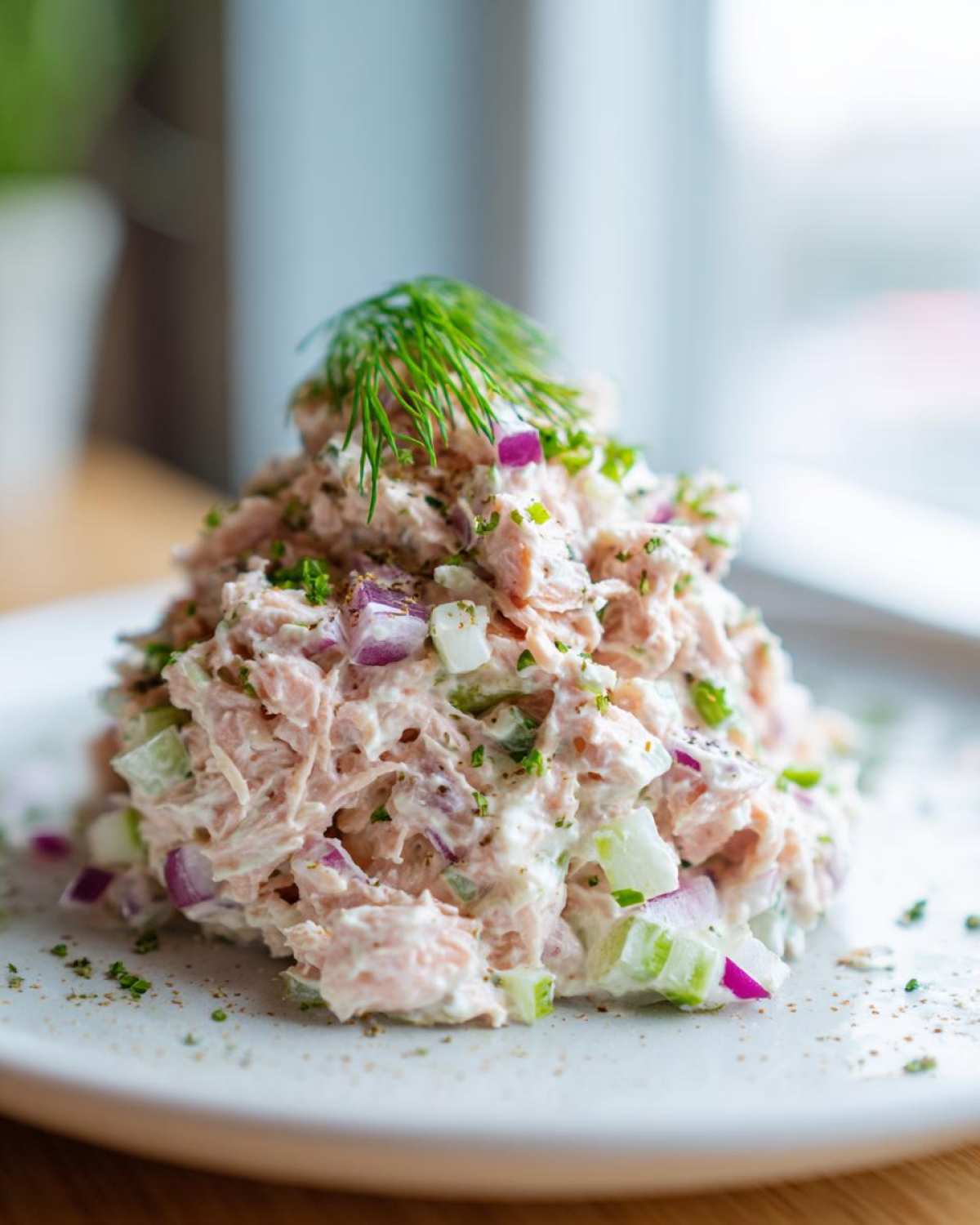 A mound of creamy salmon salad mixed with red onion and celery, topped with fresh dill.