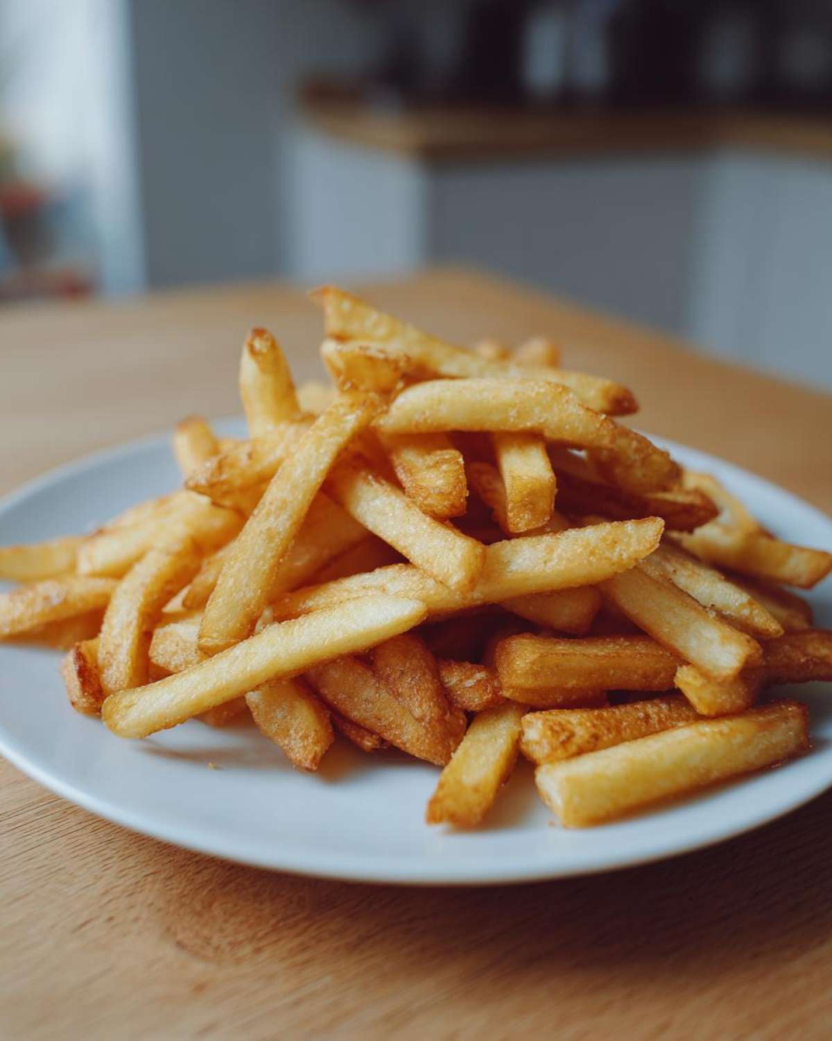 A close-up of a generous pile of perfectly golden and crispy air fryer french fries served on a white plate.