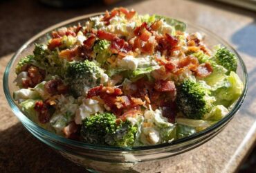 A close-up view of a glass bowl filled with Amazing 7 layer salad, topped generously with crumbled bacon.