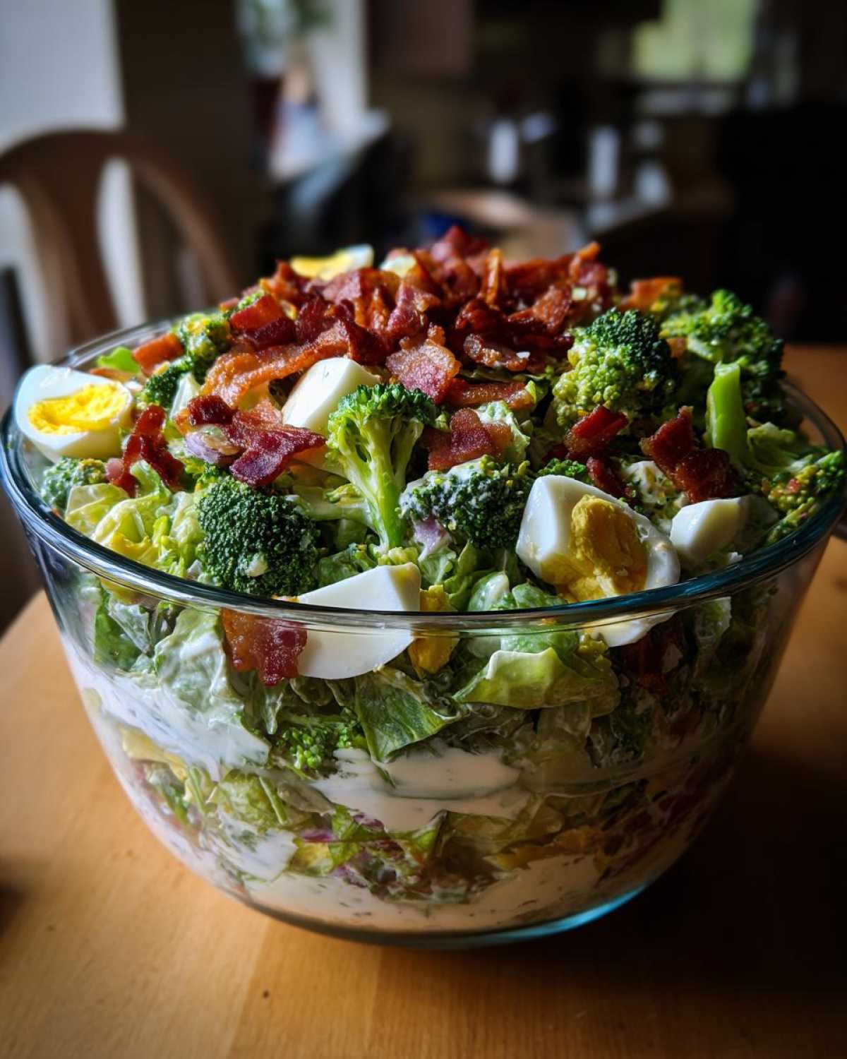 A large glass bowl filled with a colorful 7 layer salad, topped with bacon, broccoli, and hard-boiled eggs.