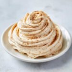 A beautiful swirl of homemade cinnamon butter, sprinkled with extra cinnamon, served on a small white plate.