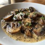 Close-up of sautéed mushroom slices generously coated in a creamy mushroom sauce, garnished with fresh parsley.