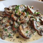 Close-up of rich, creamy mushroom sauce generously covering sliced, sautéed mushrooms, garnished with fresh parsley.