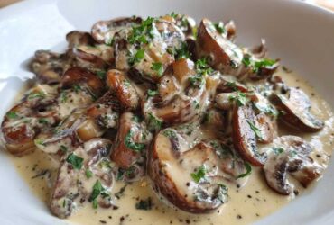 Close-up of rich, creamy mushroom sauce generously covering sliced, sautéed mushrooms, garnished with fresh parsley.