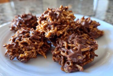 A close-up view of several freshly made chocolate haystack cookies piled on a white plate.
